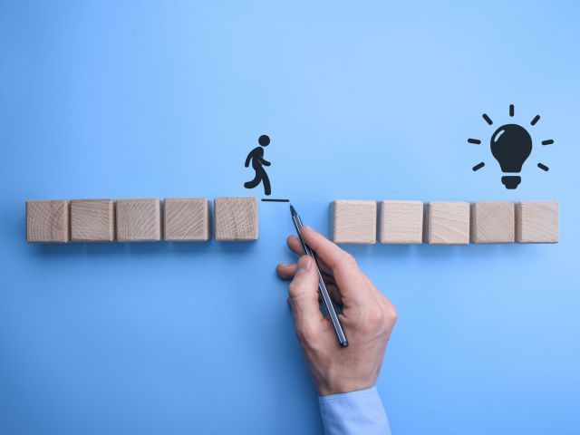 Male bussinnes man hand drawing a connecting line between two sets of wooden blocks for a silhouetted man to walk across.Conceptual of teamwork and support.